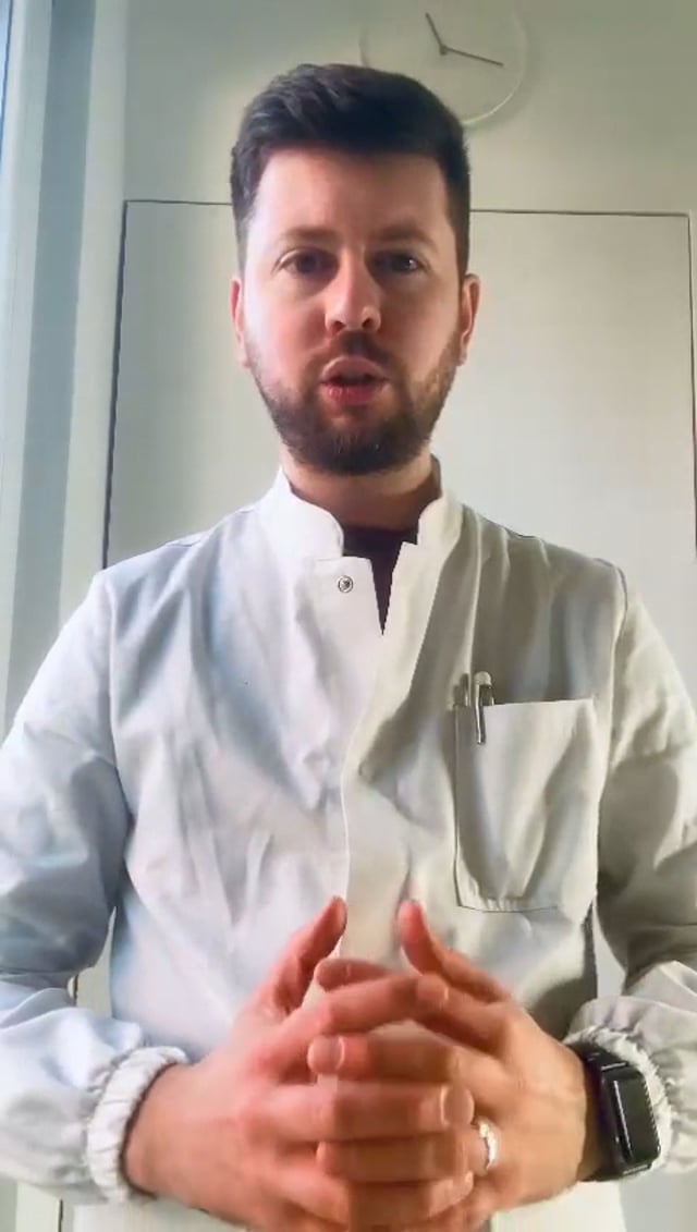Fermo immagine del video: un farmacista in camice bianco, le mani intrecciate, parla alla fotocamera.